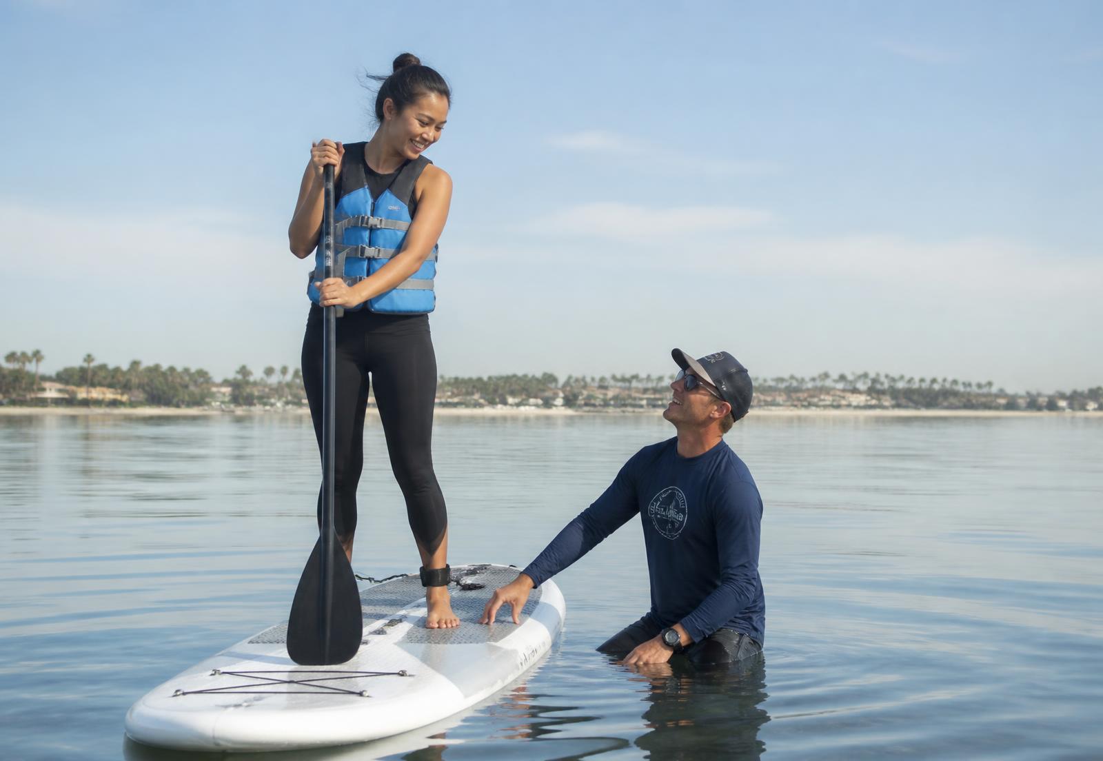 An instructor coaching a beginner on a paddleboard on flat water